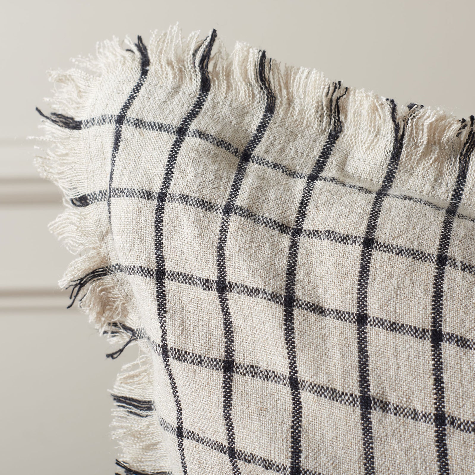 Wispy fringe and a textured weave soften the natural linen pillow's black grid || PLS8004A-2020 || detail_room