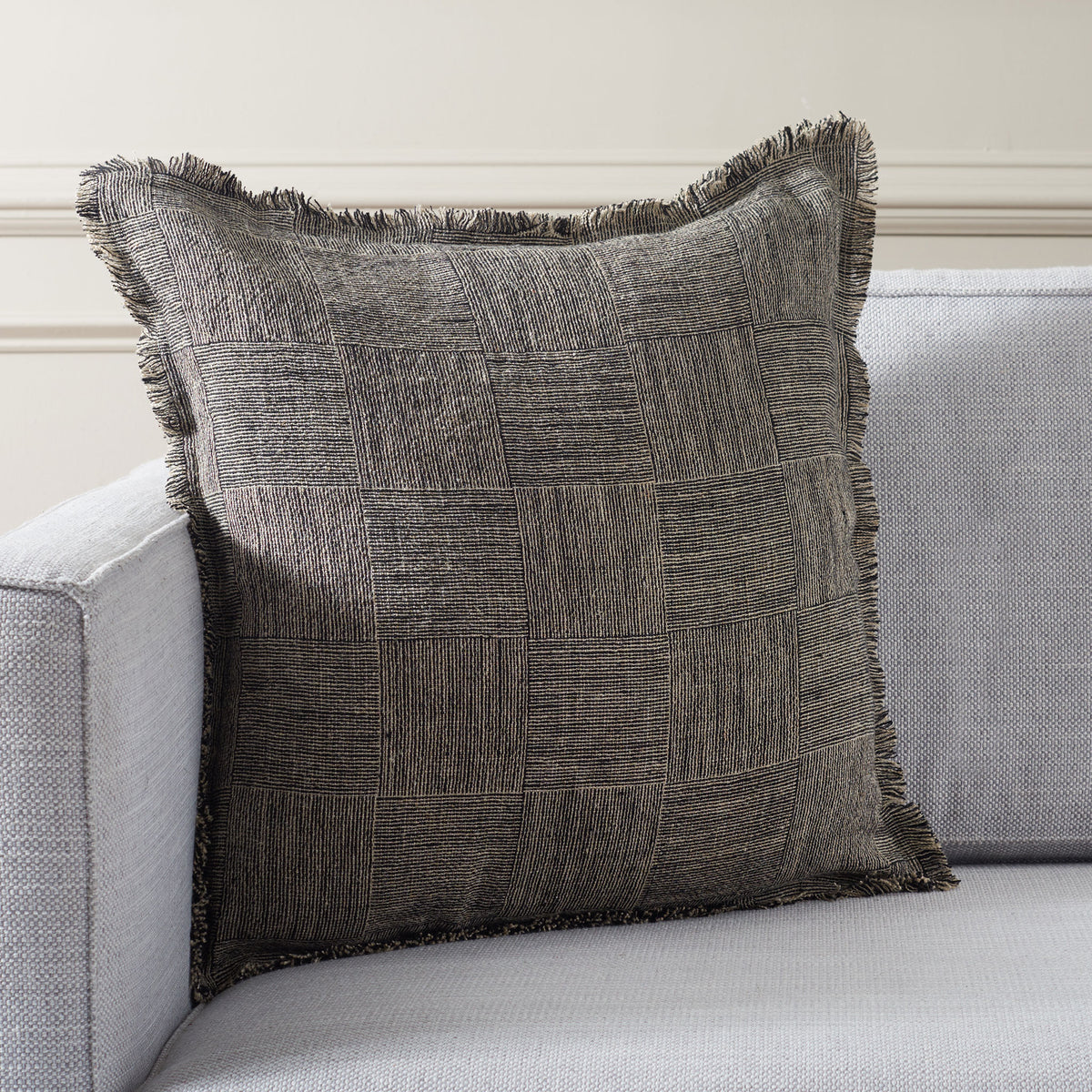 Textured square pillow adds black-and-natural pattern and playful fringe to a pale sofa. || PLS8008A-2020 || front_room