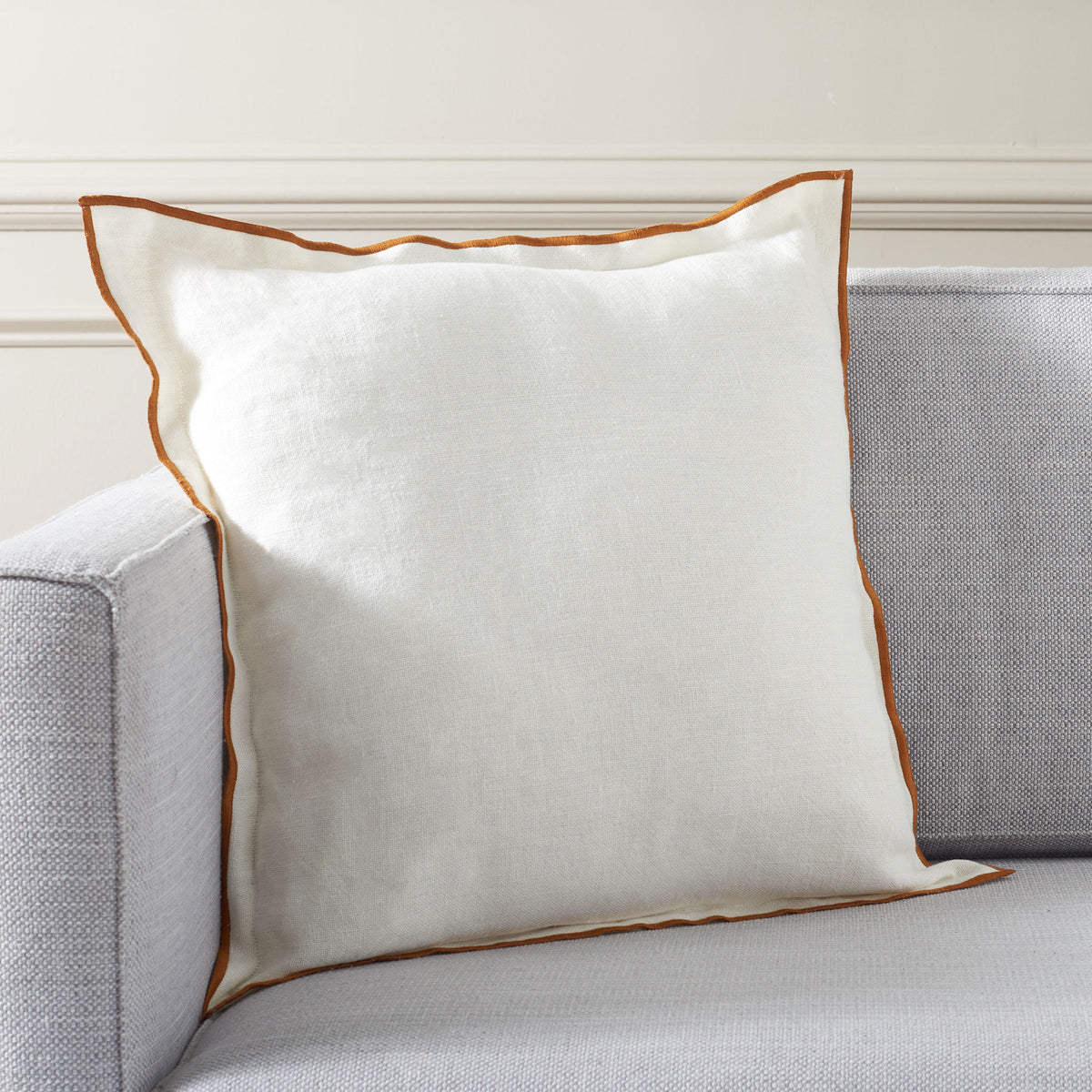 A white linen pillow with rust trim adds a warm accent to a neutral sofa.