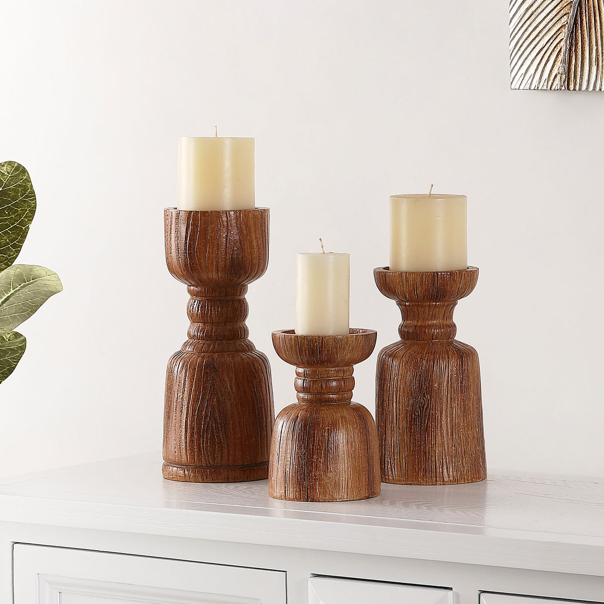 Three brown wood-look candle holders cradle ivory pillar candles in a warm, tiered display.