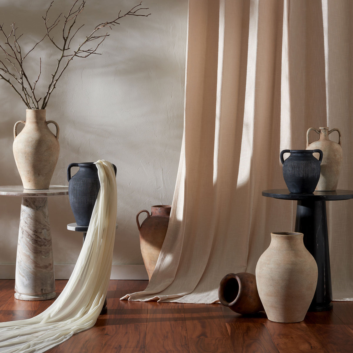 Dark ribbed vases add sculptural texture among pale pottery, soft drapery, and bare branches || RDC1210A-SET2 || front_series_room