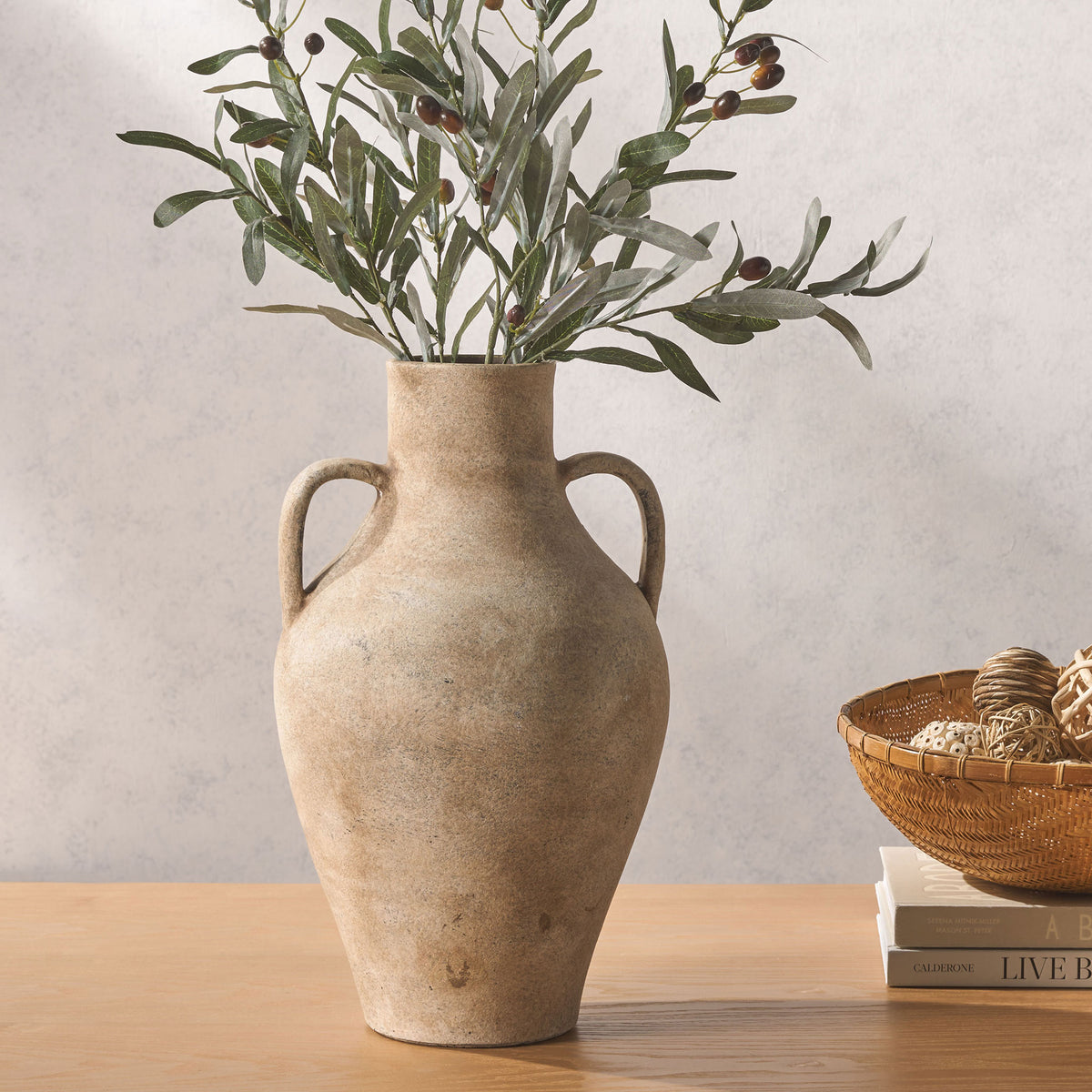 Leafy branches fill a rustic two-handled stoneware vase, bringing natural texture to a tabletop.
