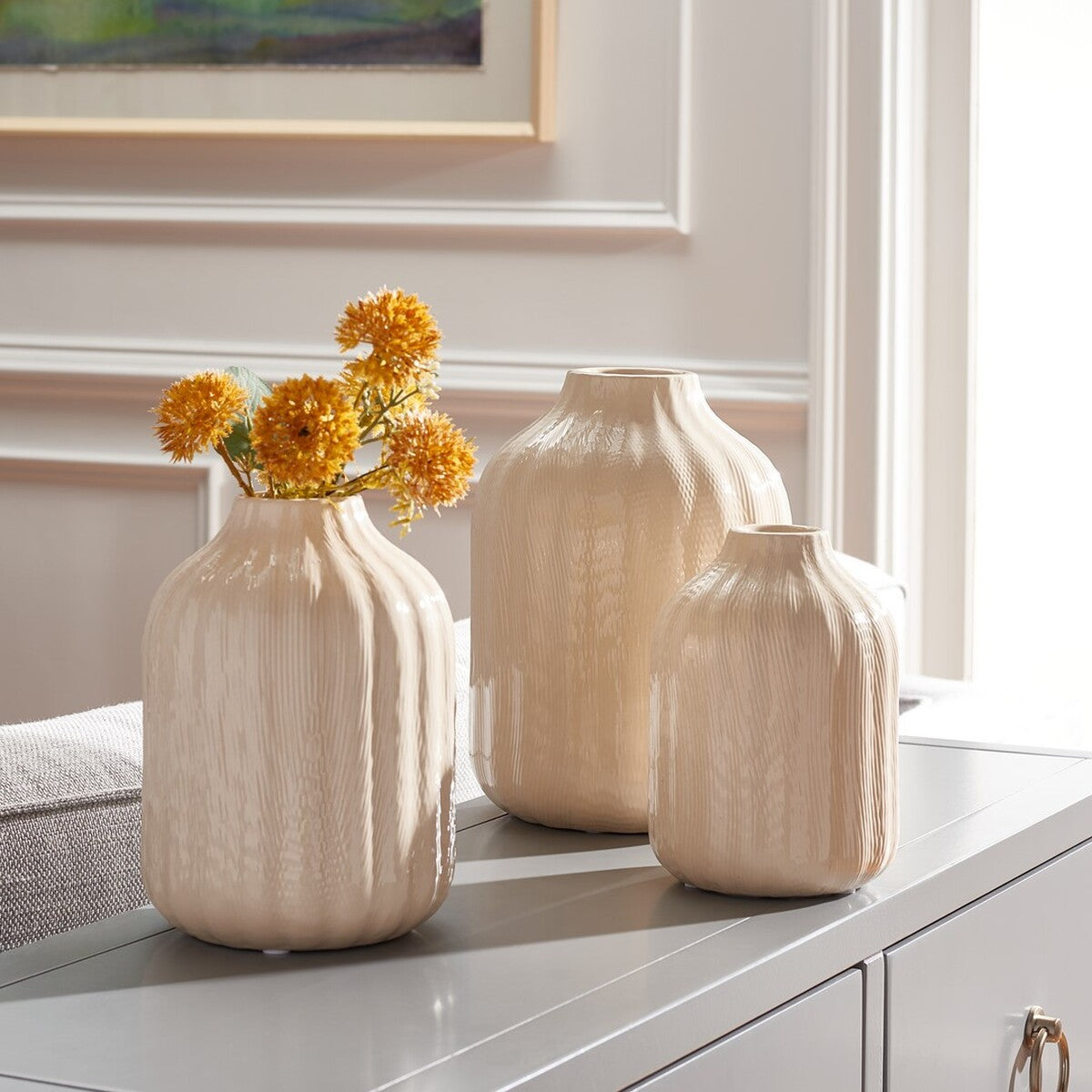 Sculptural ivory vases in three sizes brighten a tabletop, with golden blooms filling one vase.