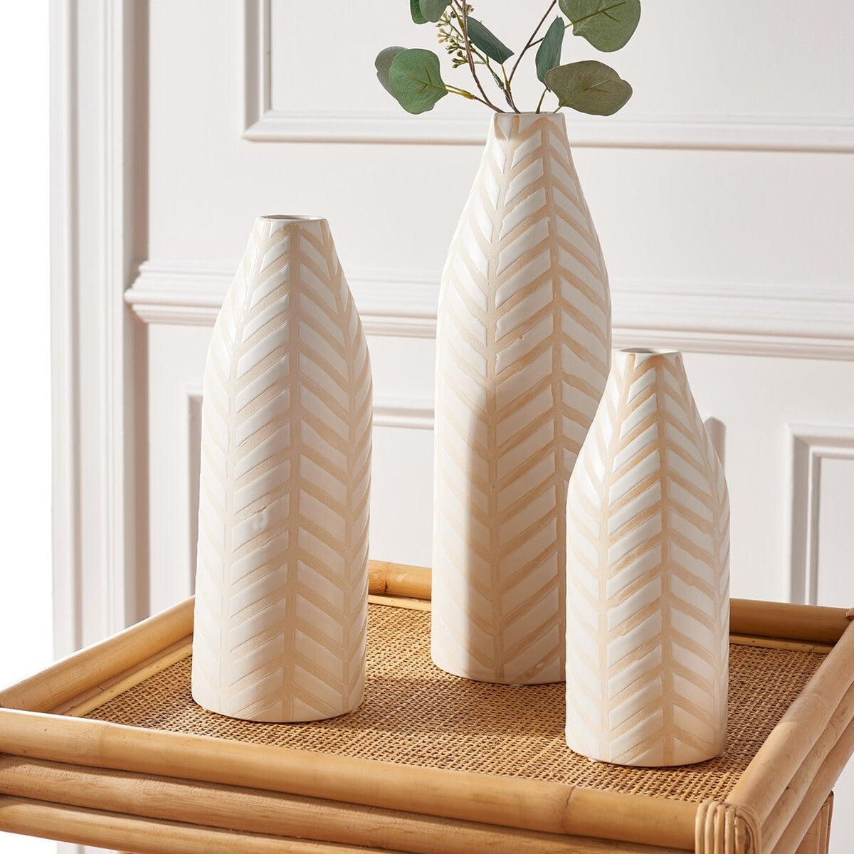 Cream vases of varying heights create a layered display with leafy greenery and embossed chevrons