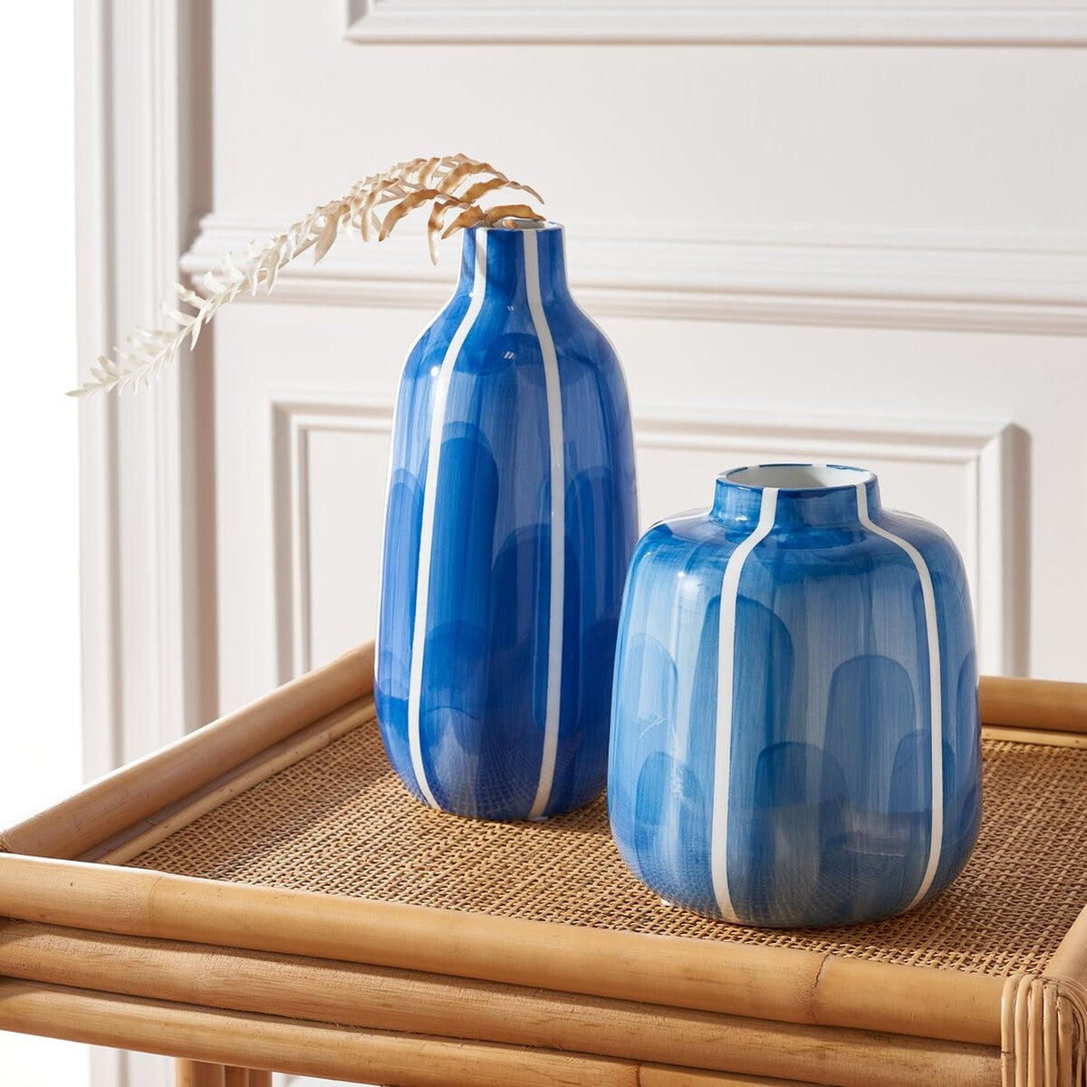 A slender blue vase and its rounded companion add sculptural color to a woven tray