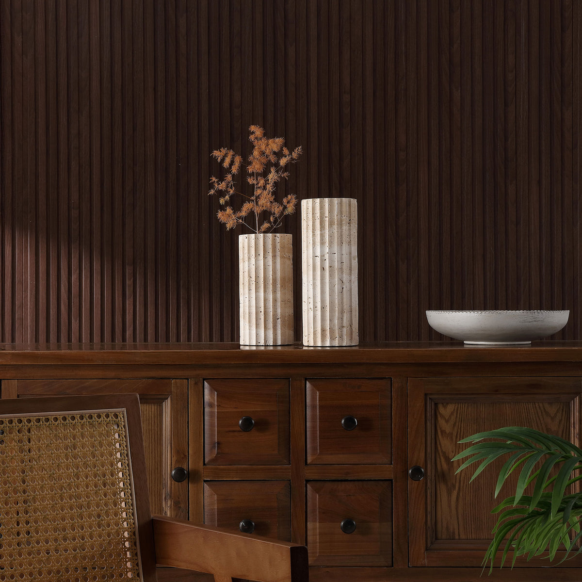 A pair of fluted travertine vases adds warm stone texture to a dark wood cabinet. || RDC4023A-SET2 || front_room