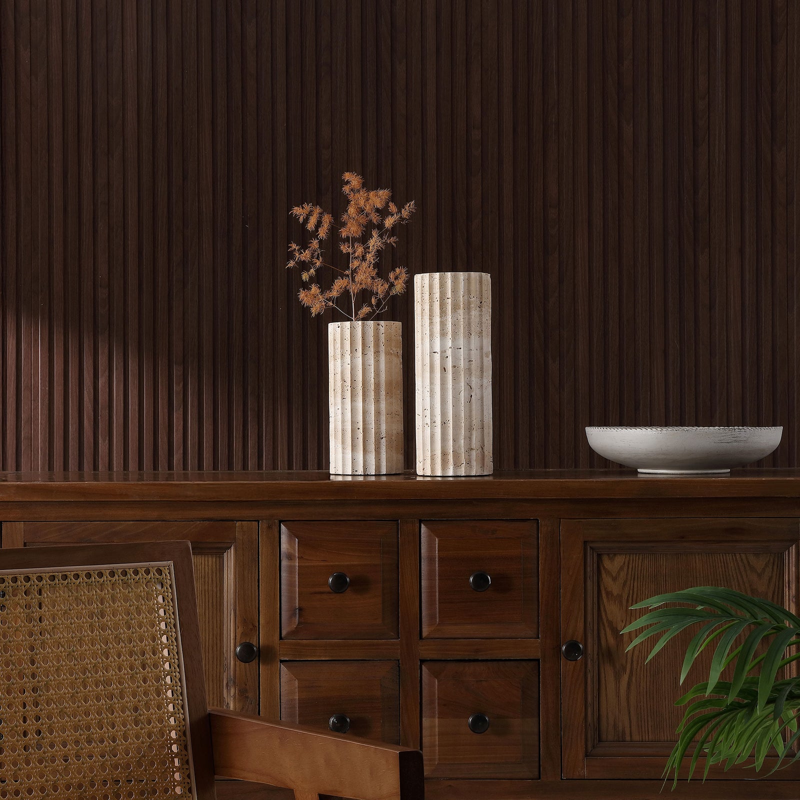 A pair of fluted travertine vases adds warm stone texture to a dark wood cabinet. || RDC4023A-SET2 || front_room