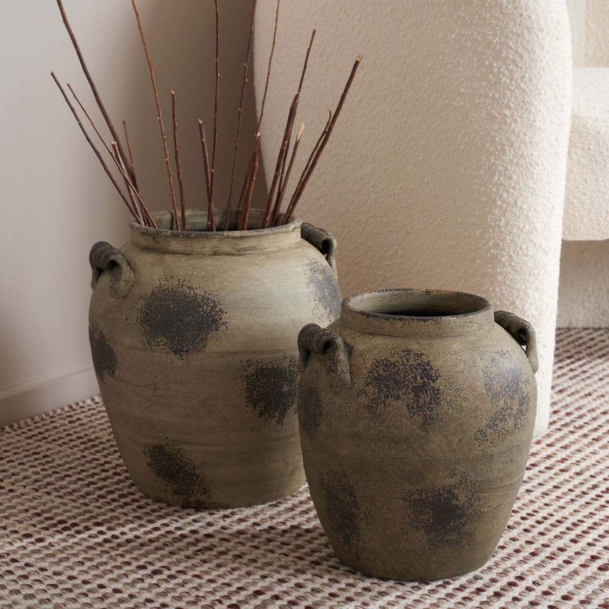 Bare branches rise from the taller of two weathered terracotta vases with dark mottled patterns. || RDC4029A-SET2 || front_angle_room