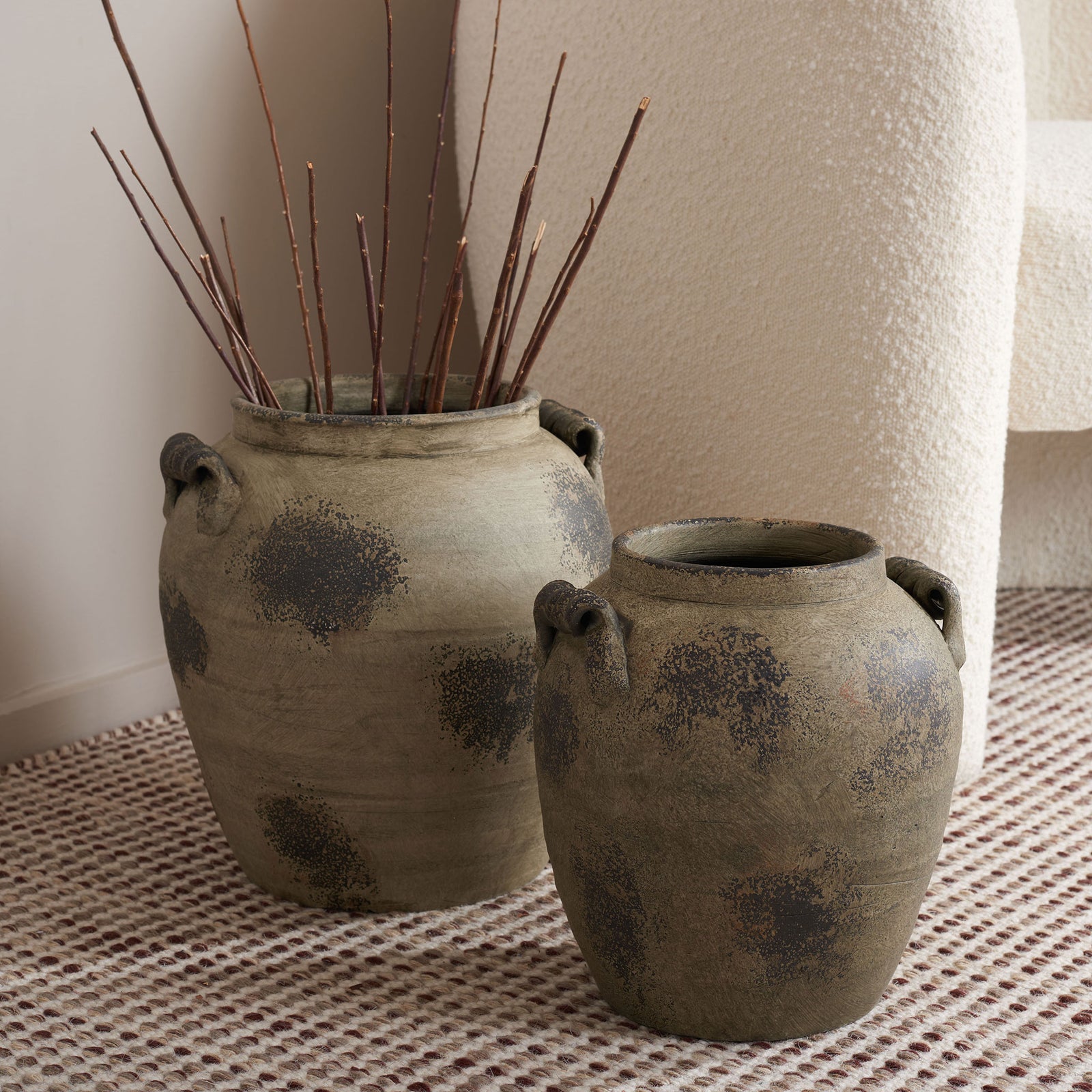 Bare branches rise from the taller of two weathered terracotta vases with dark mottled patterns. || RDC4029A-SET2 || front_angle_room