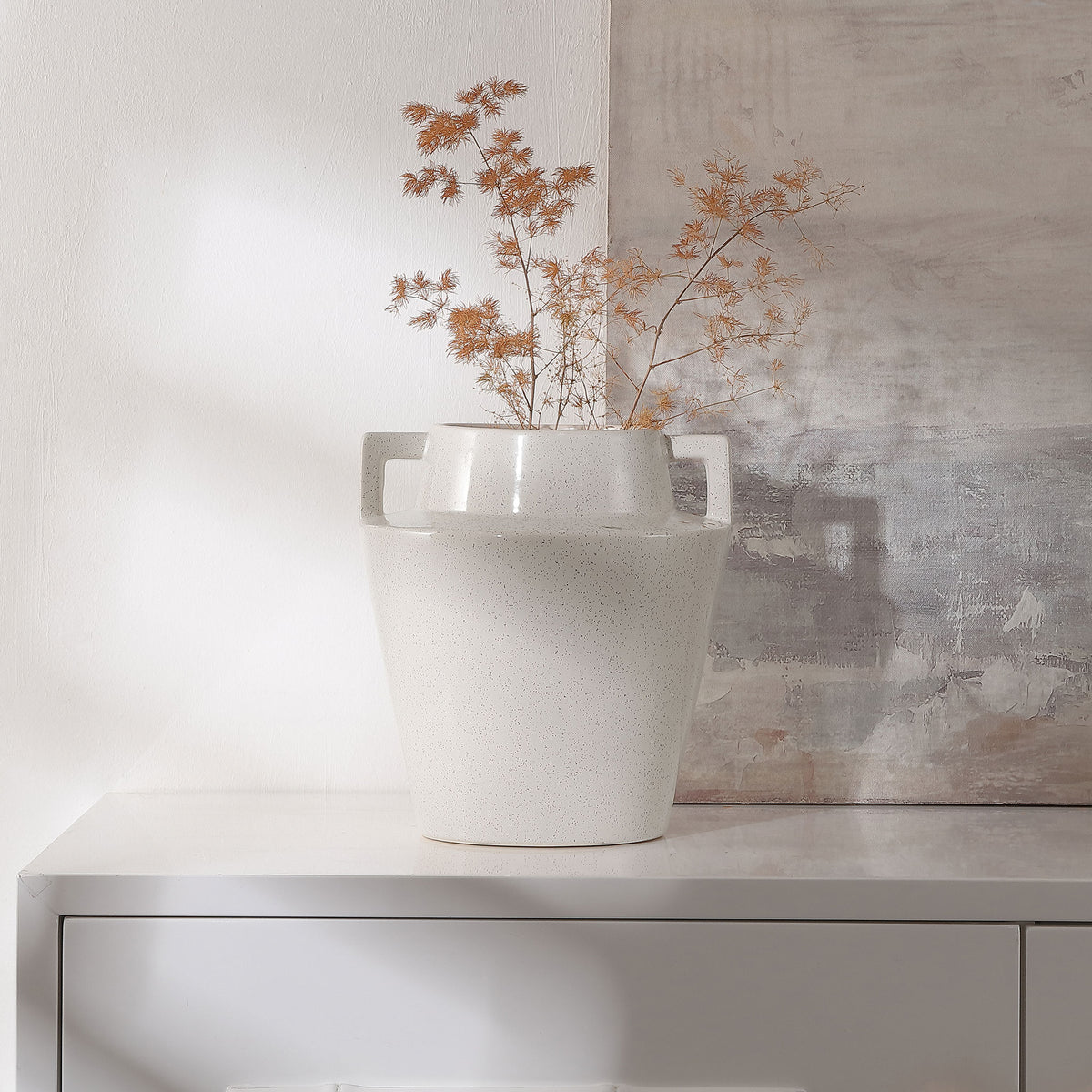 A cream speckled vase with geometric handles displays airy dried botanicals on a console || RDC4044A || front_room