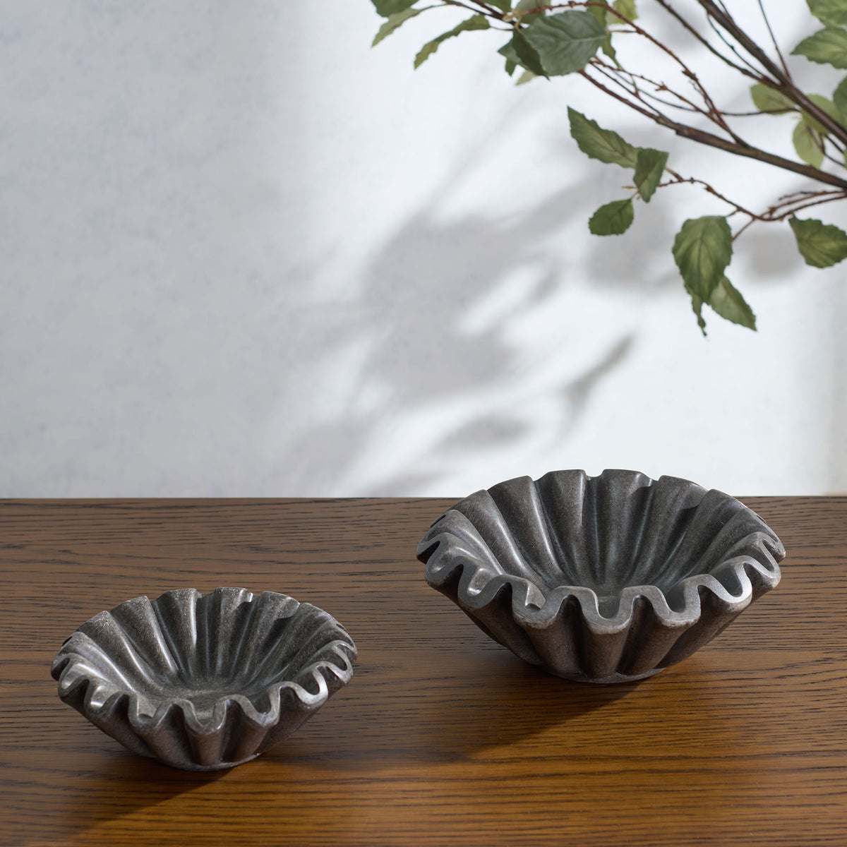 A large charcoal bowl and smaller companion display wavy edges and deep fluting on a warm wood surface.