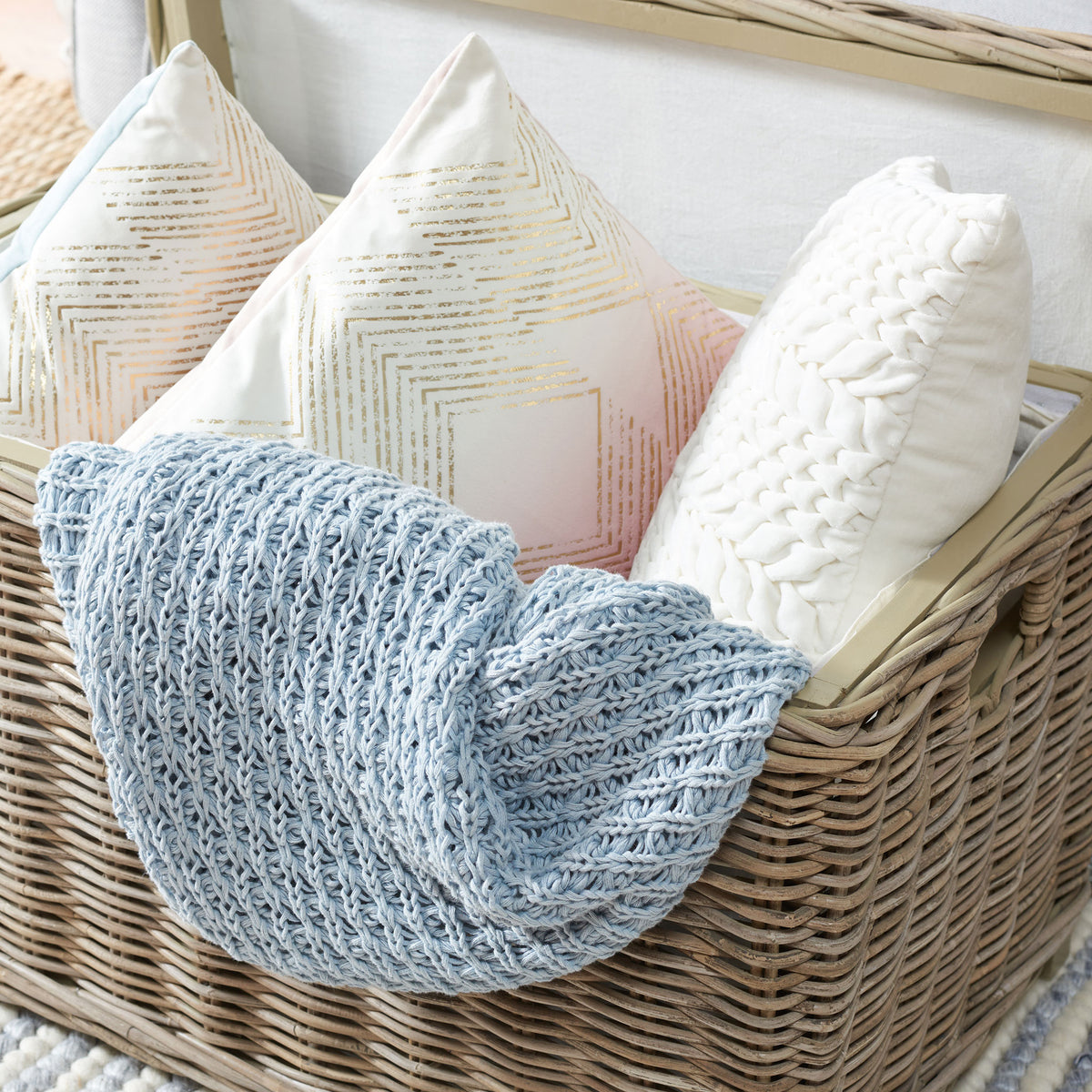 A gray rattan storage trunk keeps pillows and a blue knit throw tucked neatly inside. || SEA7018A || storage_open_room