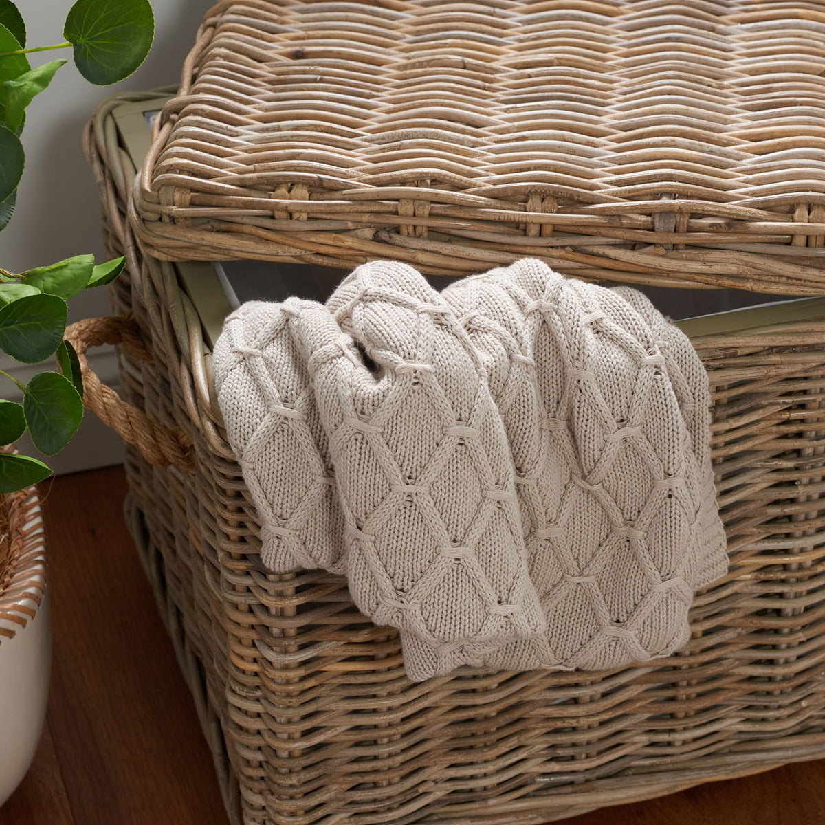 A lifted woven lid reveals roomy storage for a chunky knit throw inside the gray rattan trunk. || SEA7019A || storage_open_room