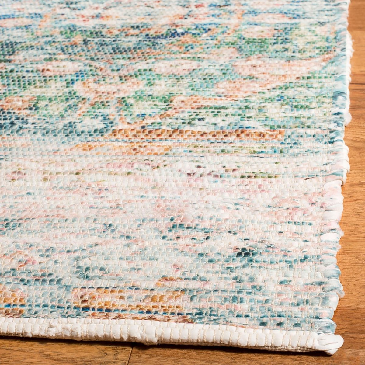 Close-up of turquoise and peach rug's textured weave and neatly bound corner on a wood floor || SFN563A-5 || corner_room