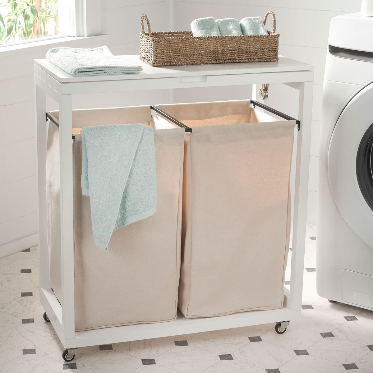A white lid provides space for folded towels above twin beige fabric laundry bins on casters. || STG1900A || front_angle_room