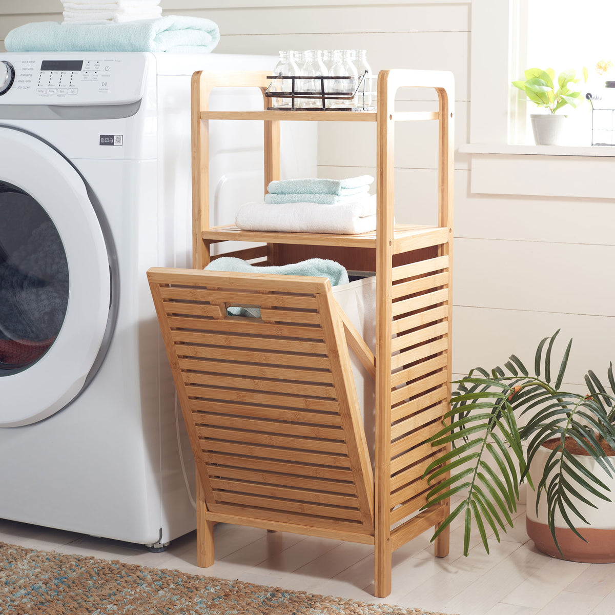 A tilt-out bamboo hamper reveals a fabric bin beneath shelves stocked with fresh towels and bottles