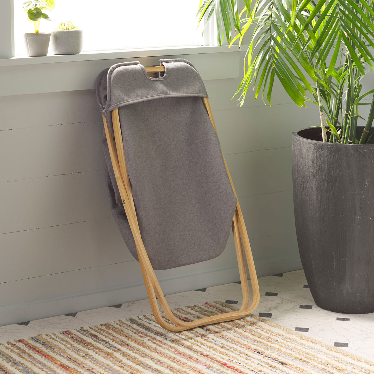 The gray fabric hamper folds against its curved bamboo frame to save space between laundry loads. || STG1906A || side_converted_room