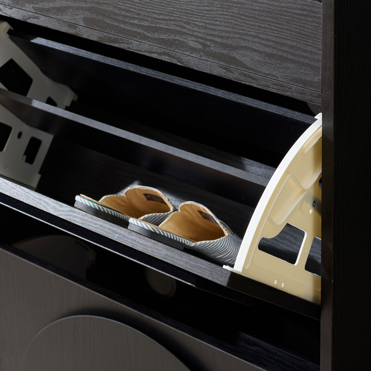 A roomy tilt-out shelf keeps slip-on shoes organized behind a black wood-grain front. || STG3100B || storage_open_room