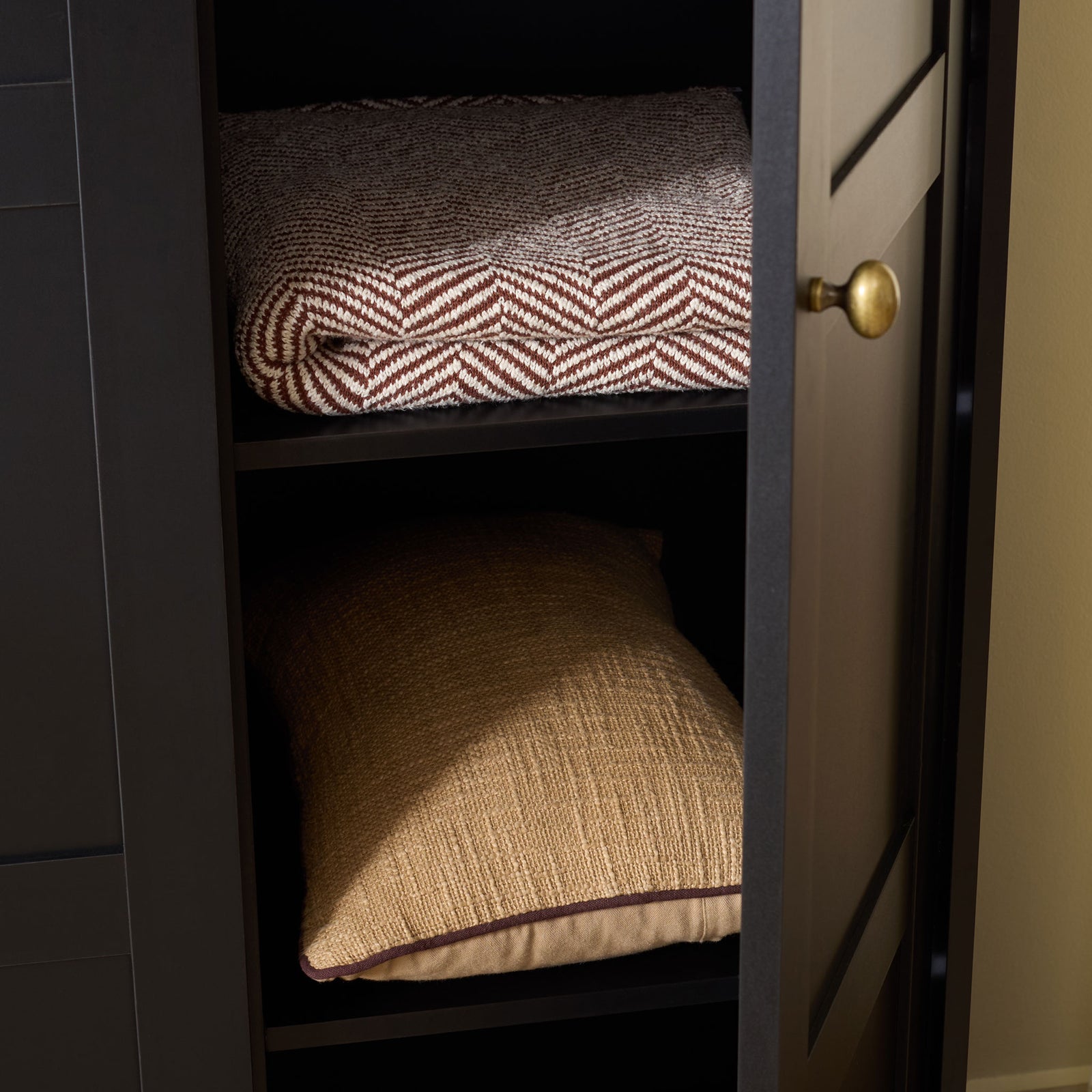 Open black shelves hold folded throws and pillows behind a paneled door. || STG3103C-3BX || storage_open_room