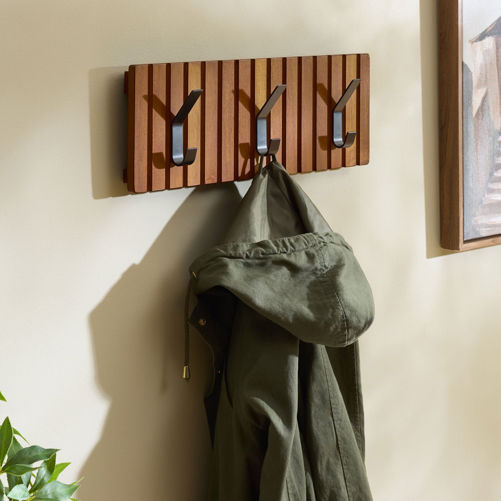 A coat hangs neatly from one of three black hooks on the slatted wood rack || STG5000A || front_angle_room