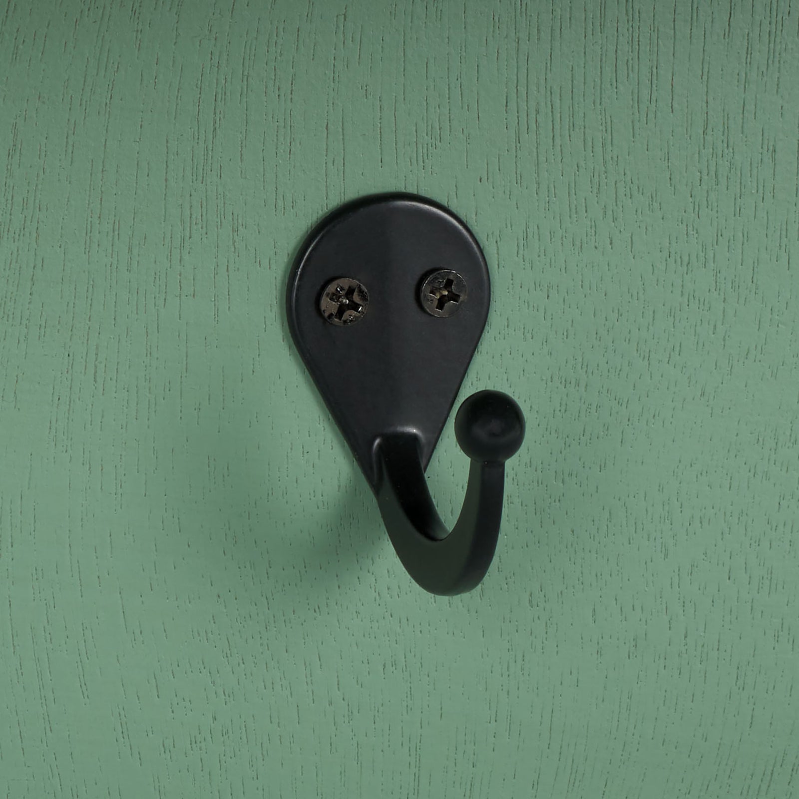 A black metal hook provides a bold contrast against softly grained sage green wood || STG5702C || detail_studio