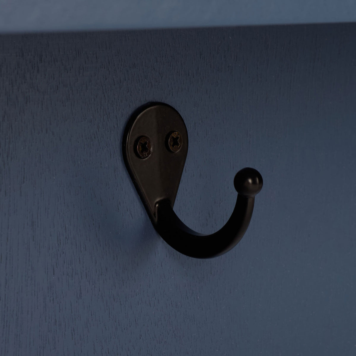 A curved black metal hook contrasts with the blue painted wood grain