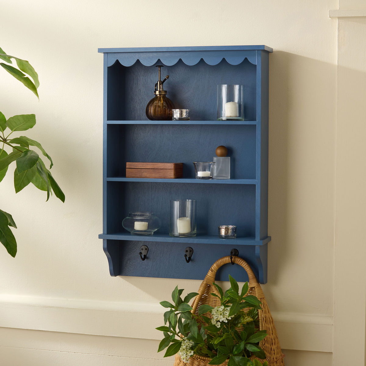 Blue wall rack holds candles and decor on three shelves, with a woven basket hung below