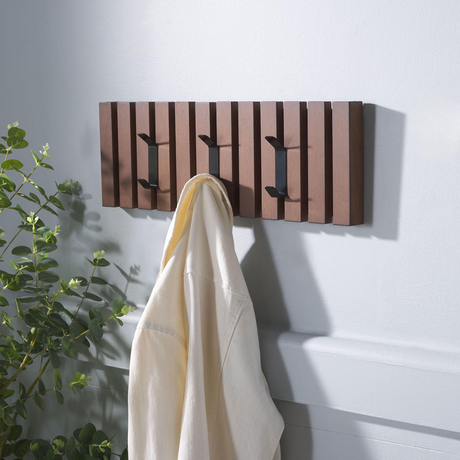 A cream robe hangs from the walnut-toned rack, with two more black hooks open for outerwear. || STG5704D || front_angle_room