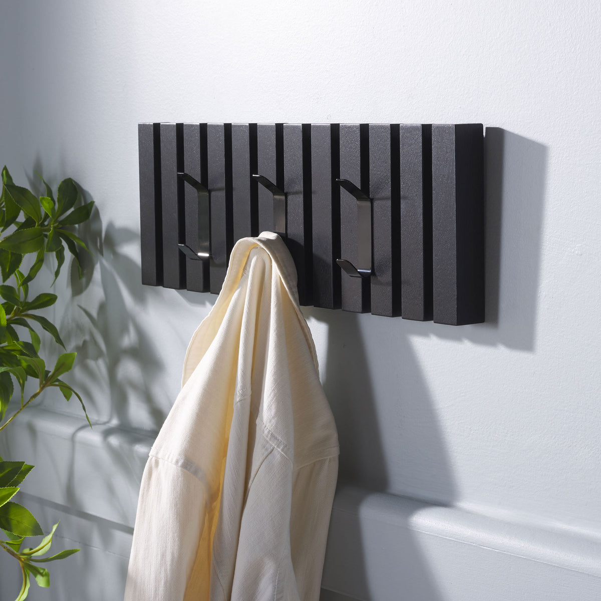 A cream robe hangs within reach on the black slatted rack, leaving two hooks open for more.