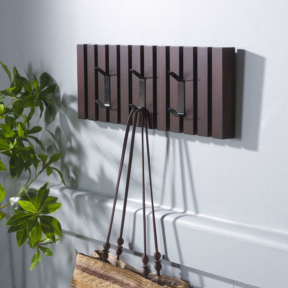 A woven tote hangs from the dark brown rack, with two more metal hooks ready for coats and hats.