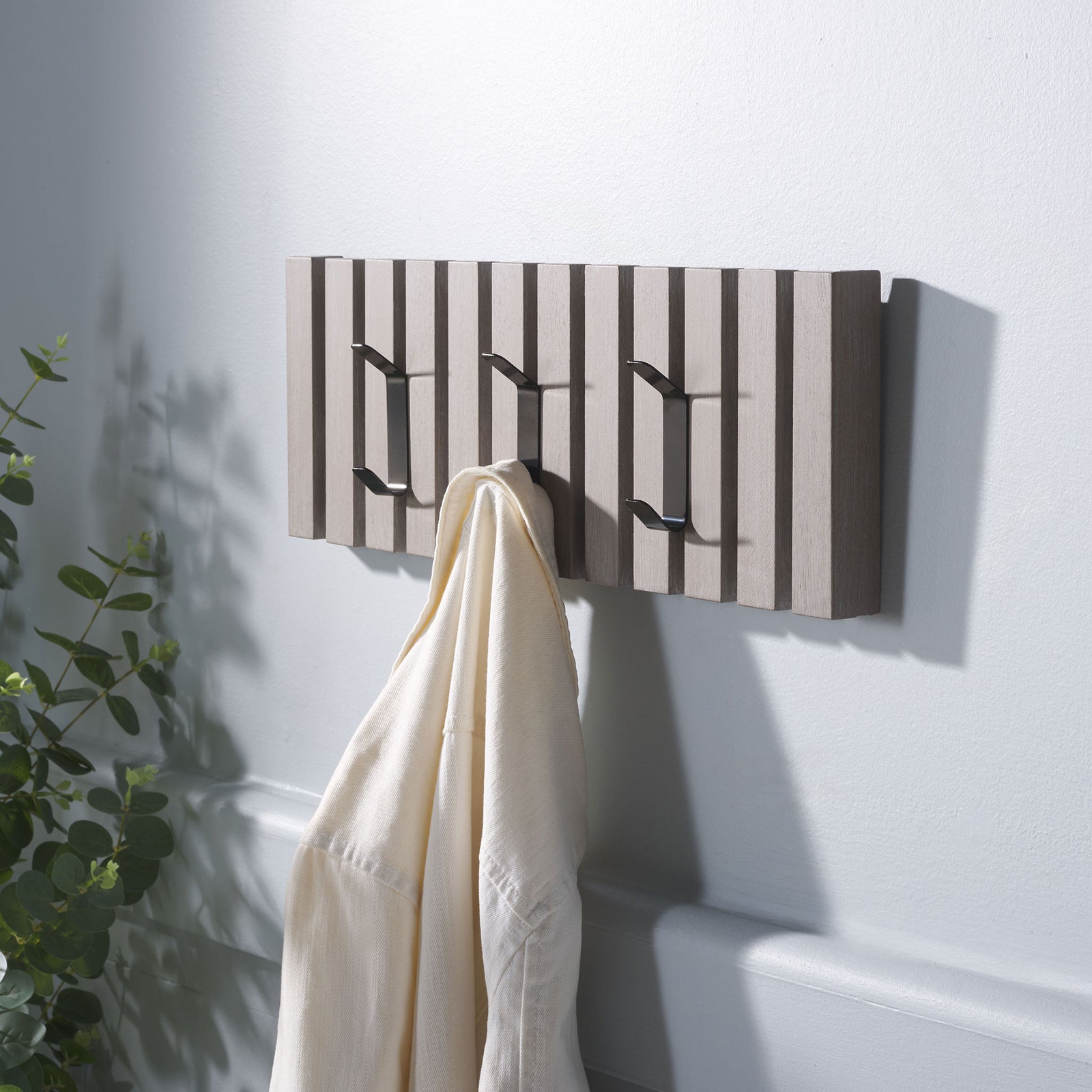 A cream robe hangs from the whitewashed rack, leaving two black hooks free for bags and jackets. || STG5704K || front_angle_room