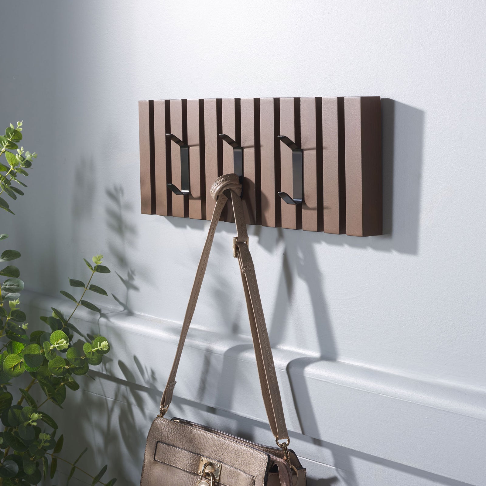 A taupe handbag hangs from one of three black hooks on the medium brown slatted rack. || STG5704M || front_angle_room