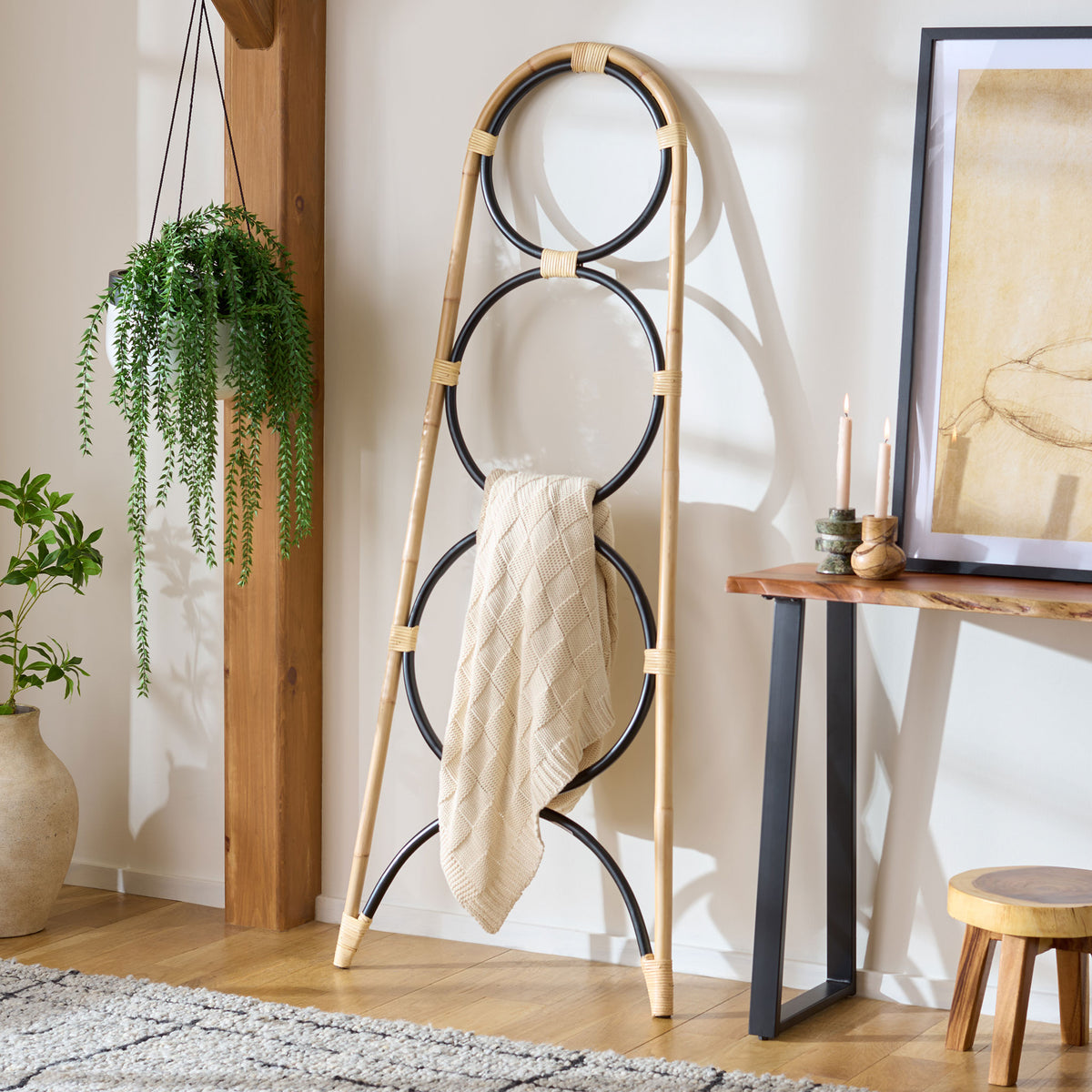 A cream knit throw hangs from the black circular rails of a natural rattan towel stand.