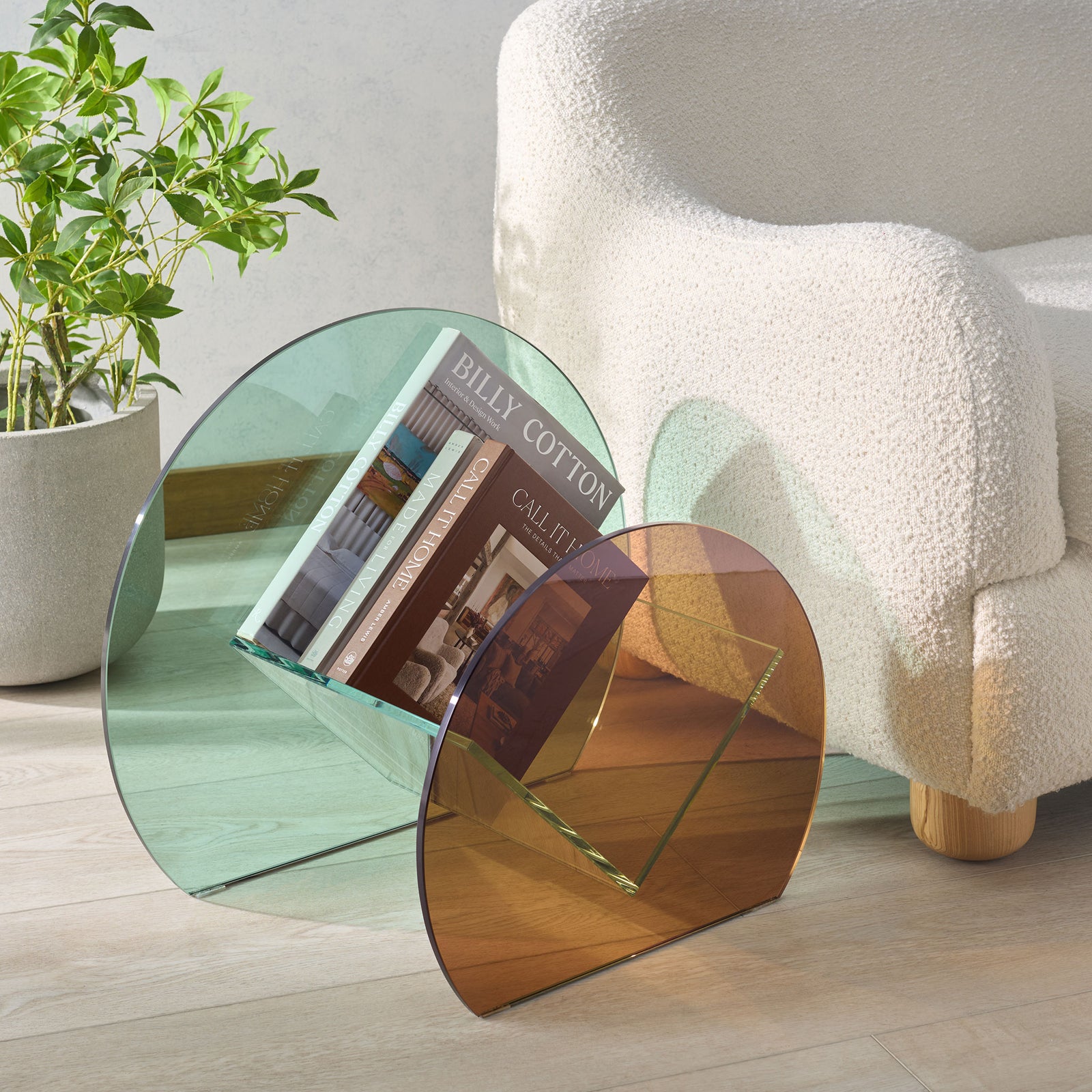 A clear glass cradle holds books between pale green and amber panels beside a cozy chair. || STG7300A || front_angle_room