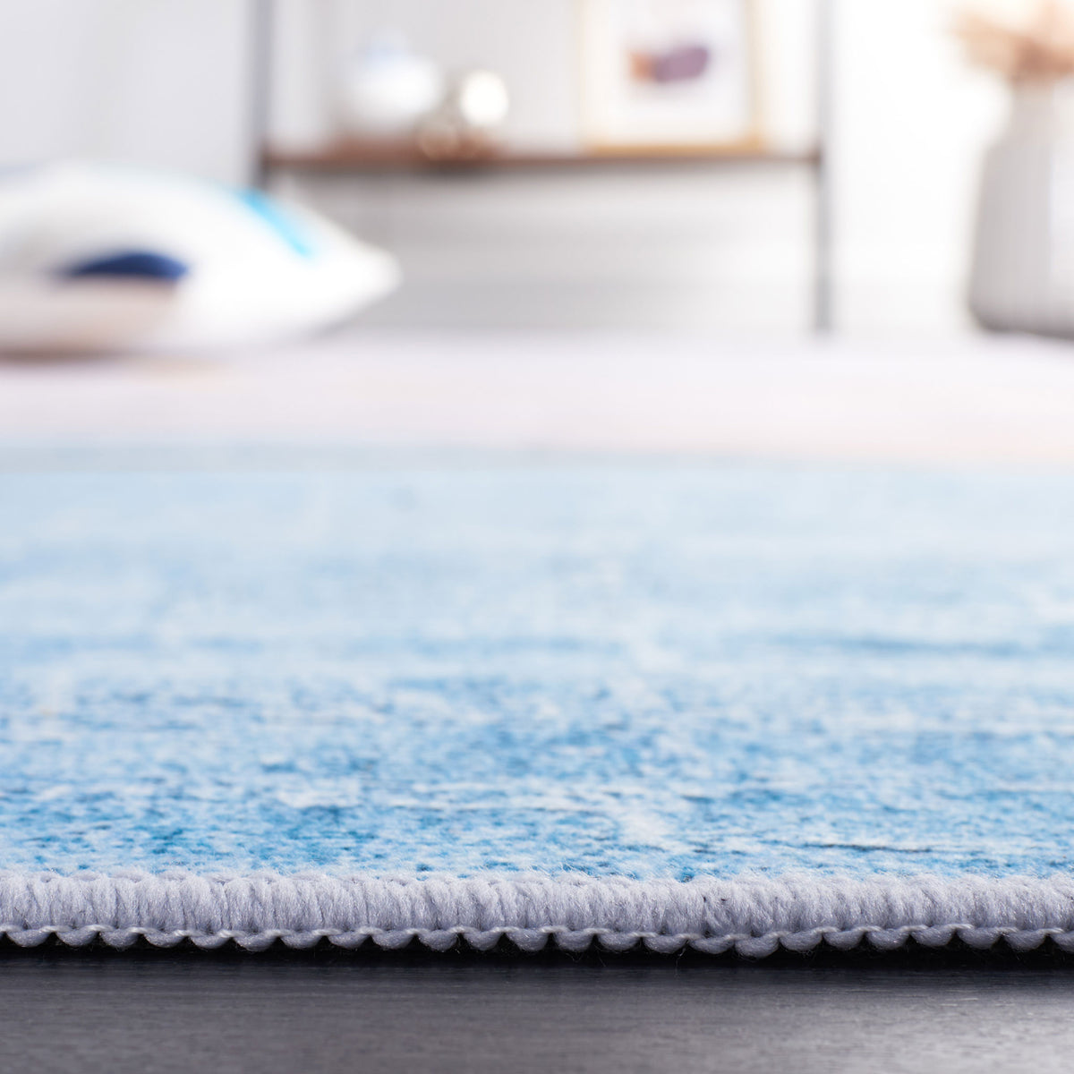 Low-profile washable rug with neatly serged edge in sky blue. || TAC834B-5 || detail_room