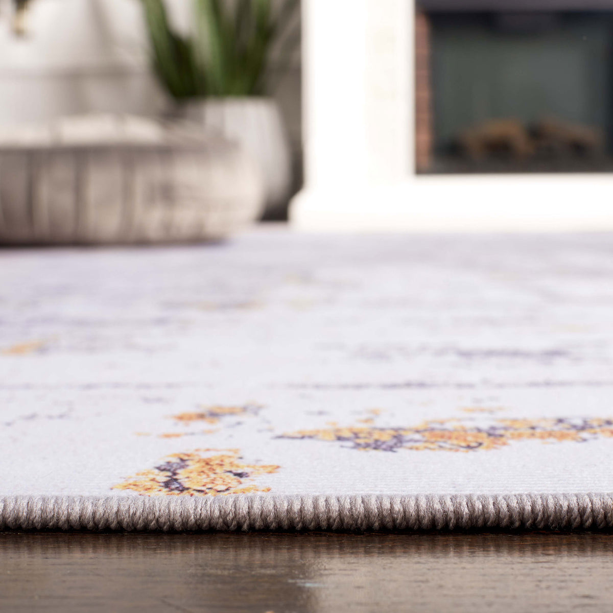 Close-up of finished edge and thin profile for easy door clearance on a patterned gray and gold rug. || TAC863F-5 || detail_room