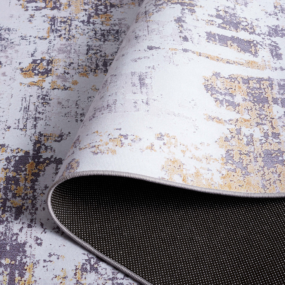 Folded rug showing dotted backing and smooth, low-profile surface in gray and gold. || TAC863F-5 || backing_studio