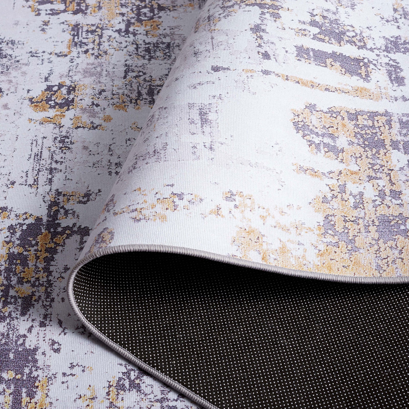 Folded rug showing dotted backing and smooth, low-profile surface in gray and gold. || TAC863F-5 || backing_studio