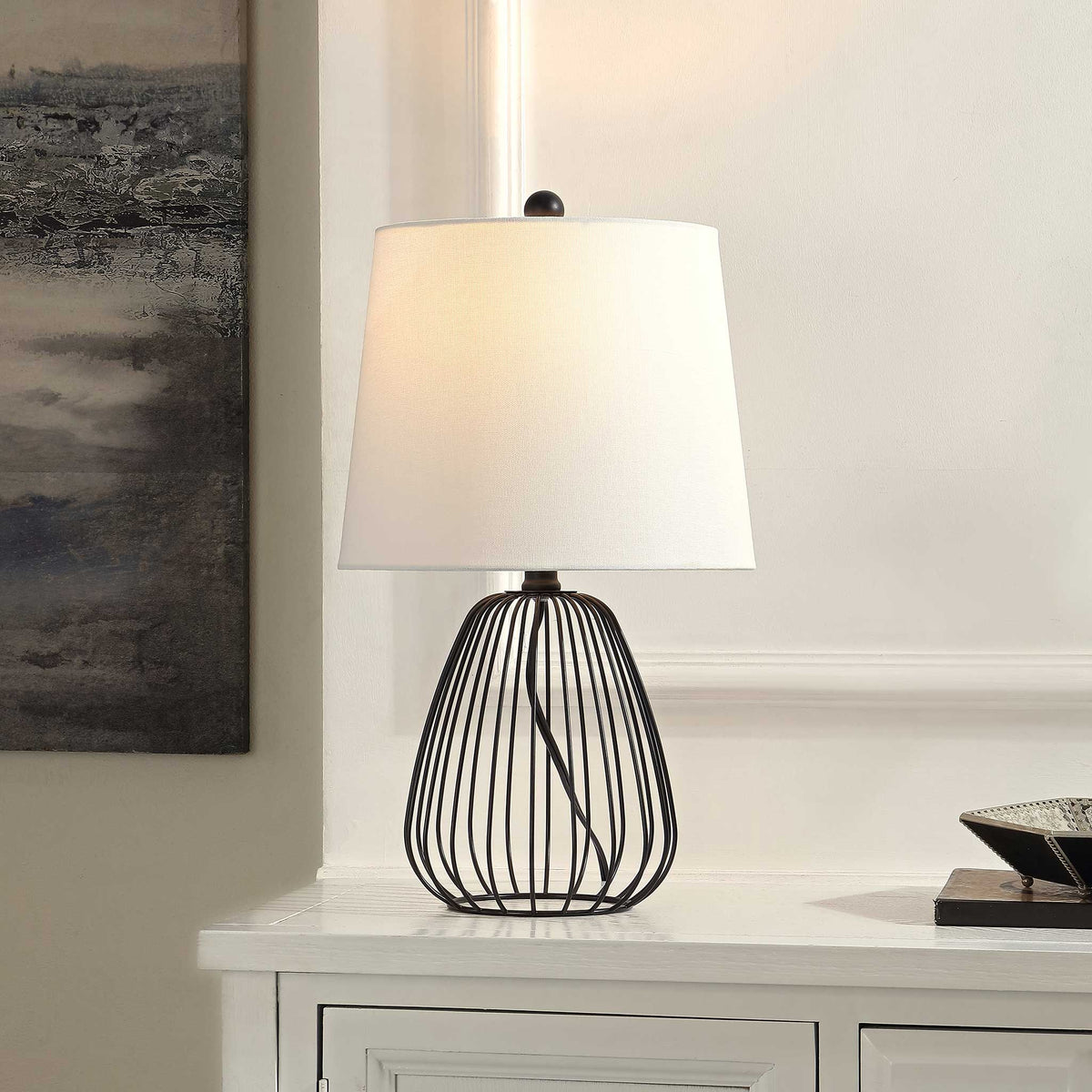 Warm glow through a white shade tops a black wireframe base for soft, sculptural style. || TBL4472A || front_angle_on_room