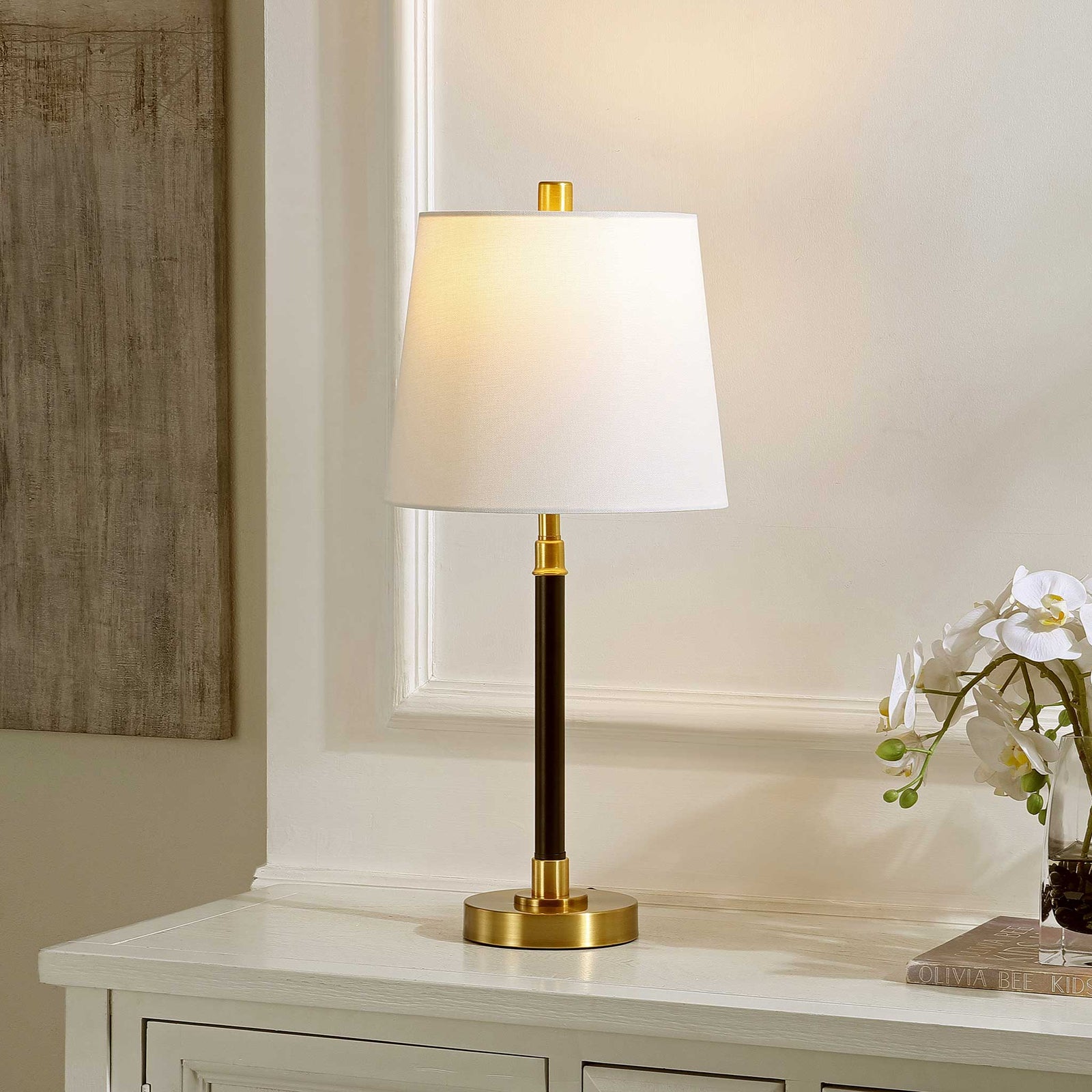 Softly lit white shade crowns a black column with brass accents, casting warm, inviting ambient light || TBL4475A || front_angle_on_room