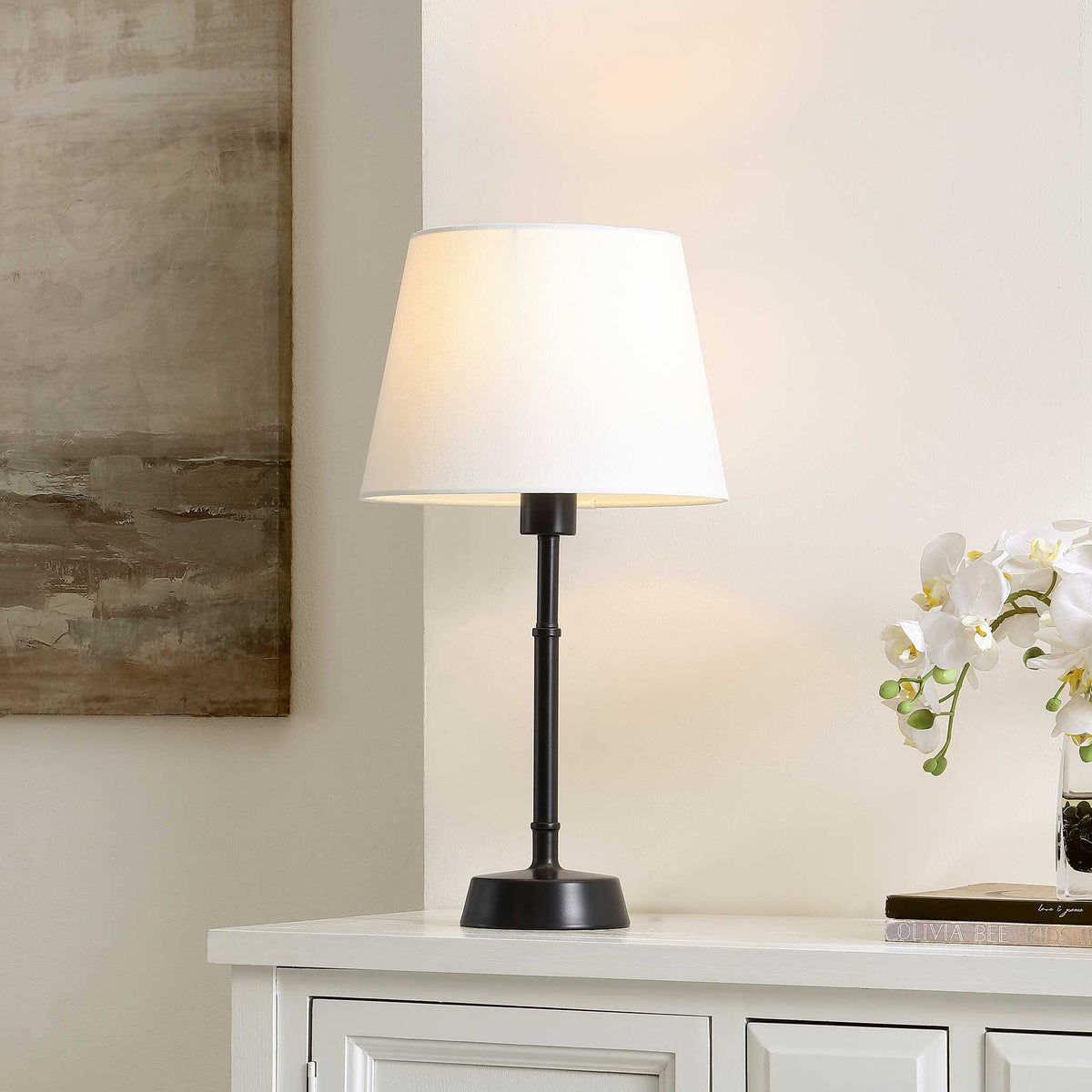 Warmly lit table lamp, white shade softly diffusing light over a refined black base || TBL4491A || front_angle_on_room