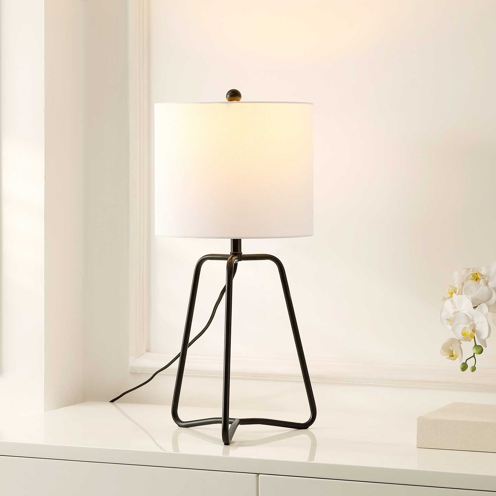 Warmly lit black iron lamp with white fabric shade, casting a soft ambient glow || TBL4498A || front_angle_on_room