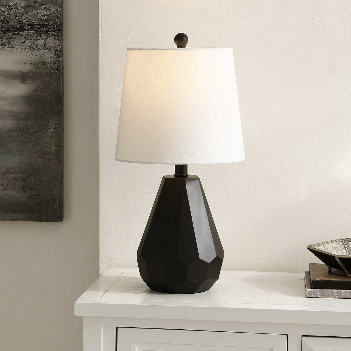 Ambient light glows through the white shade, accenting the faceted black base in a modern room. || TBL4499A || front_angle_on_room
