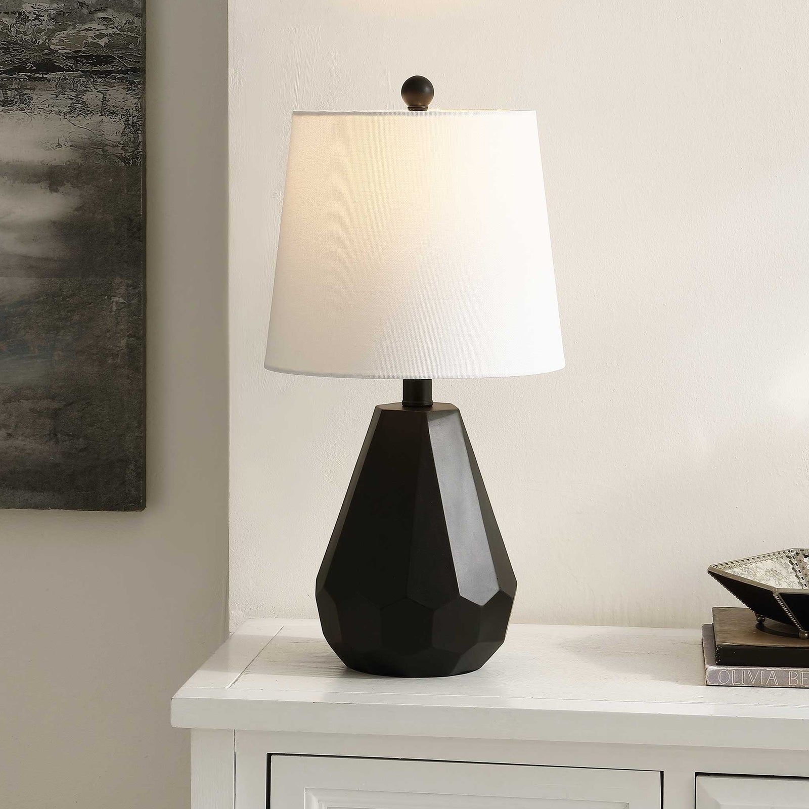 Ambient light glows through the white shade, accenting the faceted black base in a modern room. || TBL4499A || front_angle_on_room