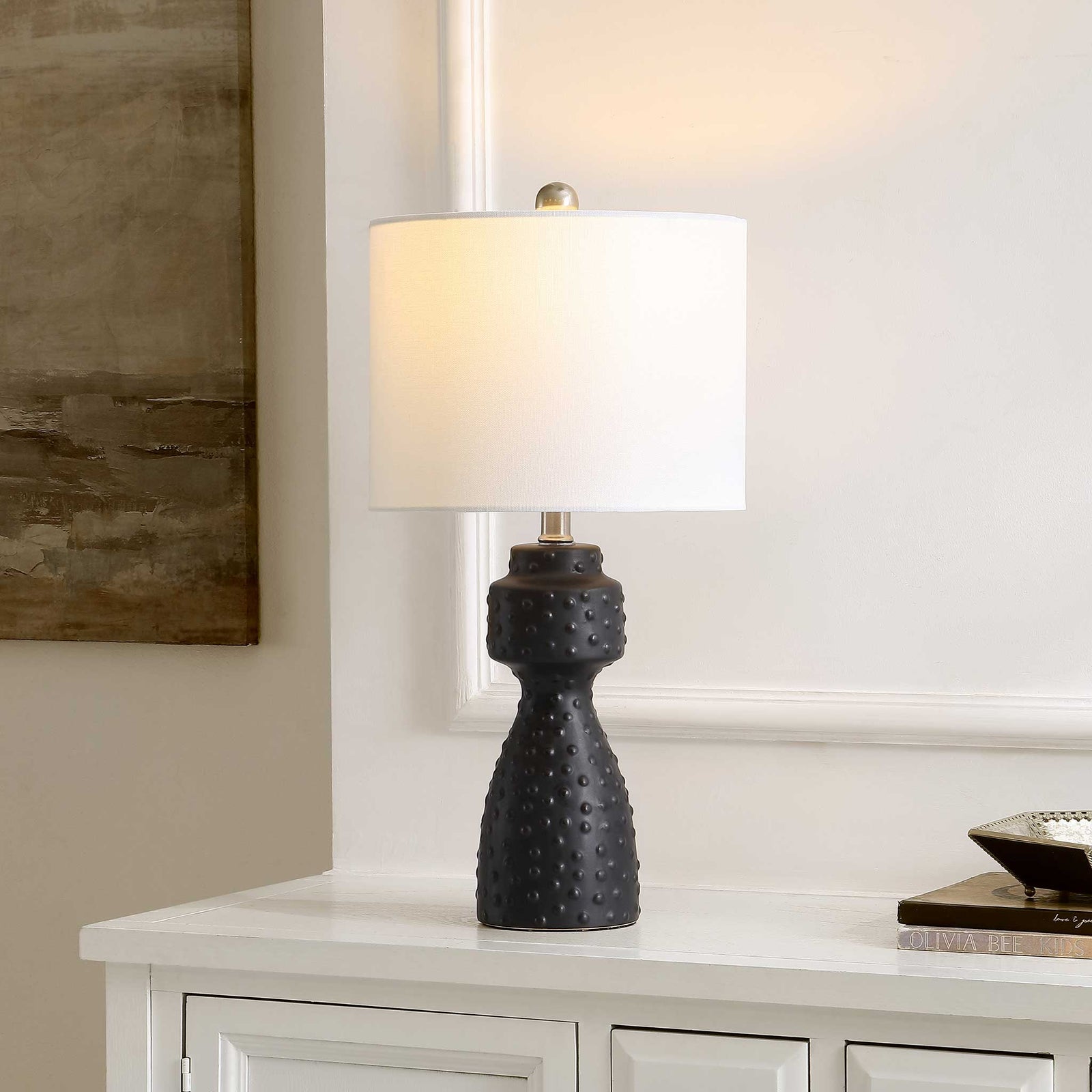 Illuminated white shade casts a soft glow above a matte black textured base || TBL4511A || front_angle_on_room