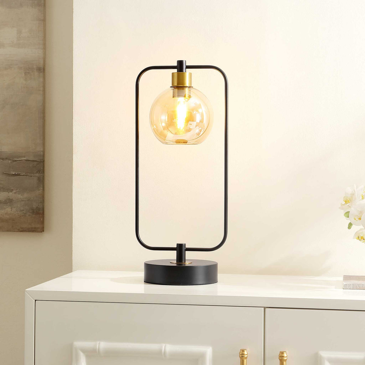 Warm amber glow shines through the globe while the black frame brings chic, modern impact || TBL4524A || front_angle_on_room