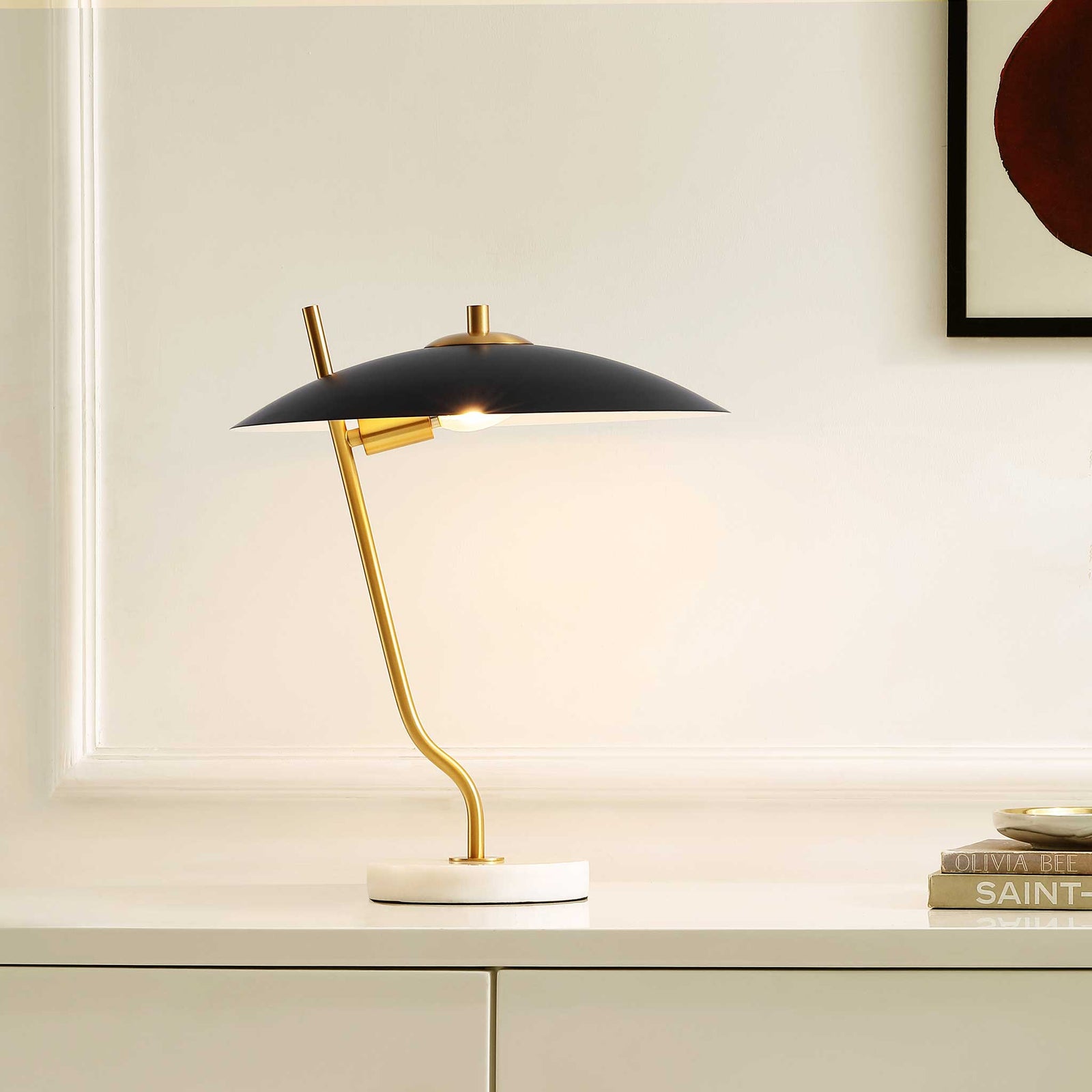 Soft light shines under a black dome shade, with a brass stem and marble base warming a contemporary space. || TBL4538A || front_angle_on_room