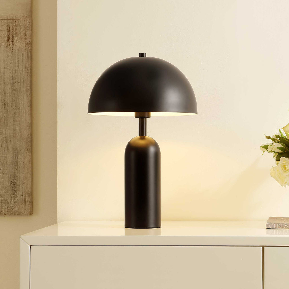 Black dome table lamp illuminating softly on a console in a warm-toned room || TBL4539A || front_angle_on_room