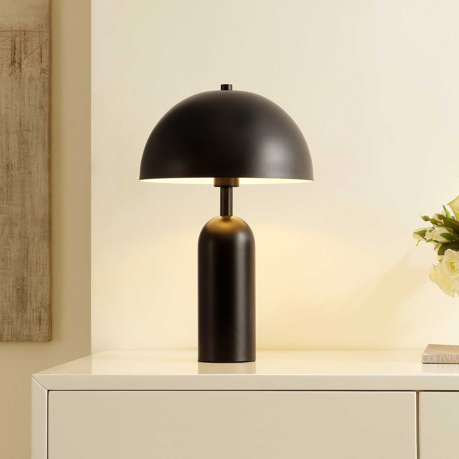 Black dome table lamp illuminating softly on a console in a warm-toned room || TBL4539A || front_angle_on_room