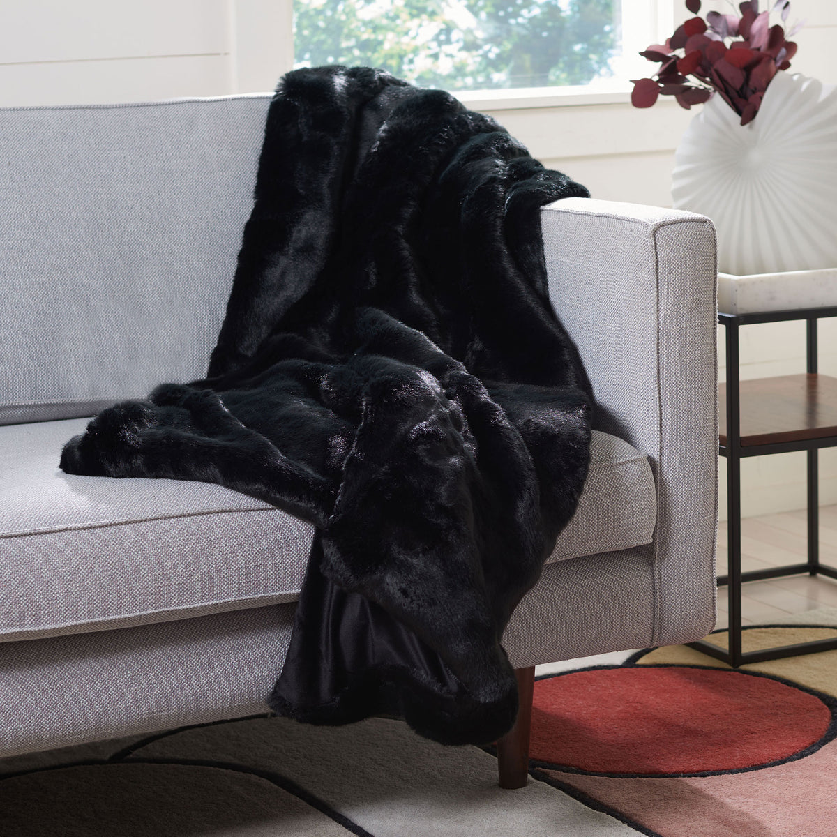 Glossy black faux fur creates generous, cozy folds across a sofa.